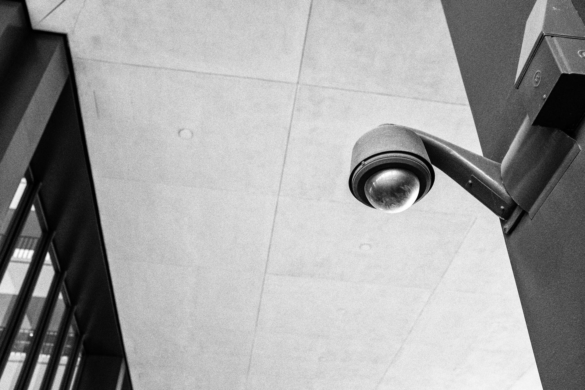 A dome surveillance camera mounted on the underside of a concrete building.